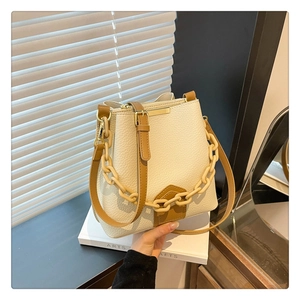 Détail d'un sac seau crème avec bandoulière en cuir brun et chaîne acrylique sur un livre