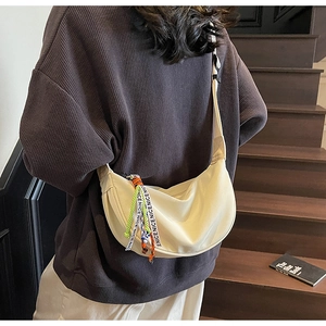 Close-up of cream half-moon crossbody bag with decorative 'NICENICE' strap on a model