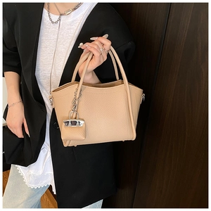 Close-up of beige lychee leather bucket bag with mini handbag charm on model