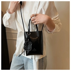 Detail view of mini black patent leather bucket bag with gold logo and bear charm