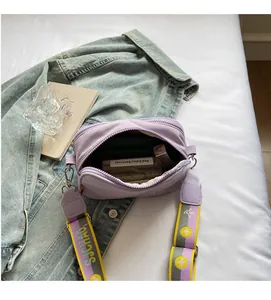 Detail of a purple nylon crossbody camera bag with wide floral strap and interior capacity