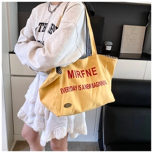 Detail view of yellow canvas tote bag with red lettering and striped lining texture