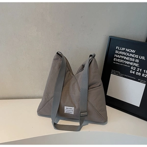 Detail of grey nylon crossbody bag showing the woven label and adjustable wide shoulder strap