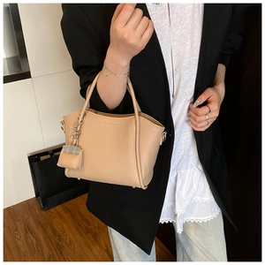 Detailed close-up of beige lychee grain leather handbag with silver chain and mini pouch