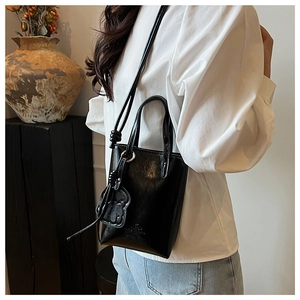 Chic black mini bucket bag with glossy finish and cute bear charm in a lifestyle setting