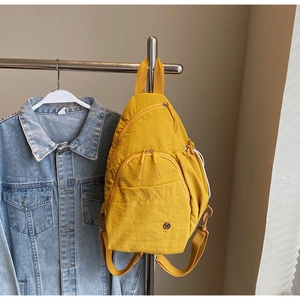 Detail of a ginger yellow nylon backpack with multiple zippered pockets and textured fabric