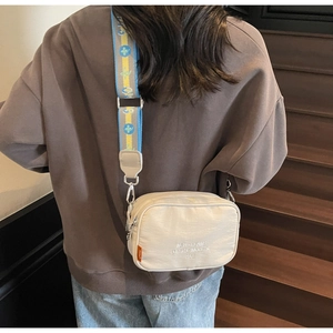 Detail of beige camera bag with embroidered text and colorful jacquard shoulder strap