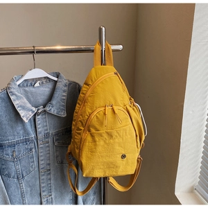 Detail of yellow nylon backpack with multiple pockets and circular logo on metal hanger
