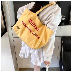 Detail of yellow canvas tote bag with red lettering and durable shoulder straps