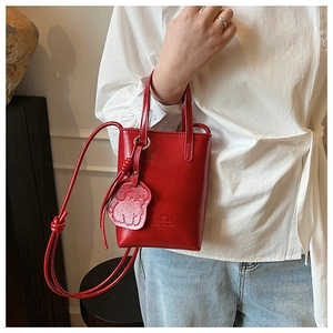 Detail of red glossy leather mini bucket bag with cute dog charm and knot shoulder strap