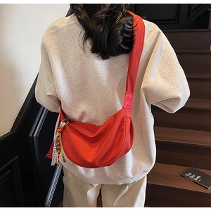 Close-up of red crescent nylon shoulder bag with a 'NICE' ribbon on the zipper