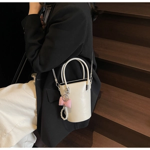 Detail einer cremeweißen Leder-Beuteltasche mit rosa Karo-Schleife und Perlenanhänger