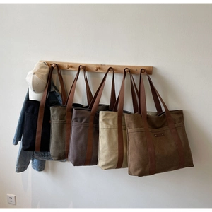 Détail de divers sacs cabas minimalistes en toile suspendus sur un support en bois