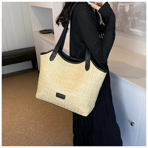 Detail of large straw tote bag with black leather accents and woven texture on shoulder