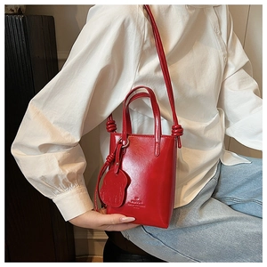 Detail of red glossy mini bucket bag with bear charm and adjustable shoulder strap