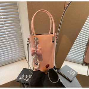 Rosa Eimertasche mit Seidenschleife und Perlenanhänger vor einem Spiegelhintergrund
