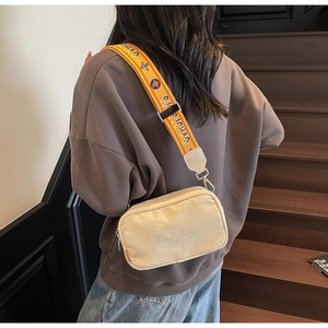 Detail of off-white canvas camera bag with New Dreams embroidery and patterned strap