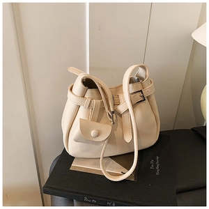Detail of a creamy white leather handbag with multi-pockets and a mini charm on a book