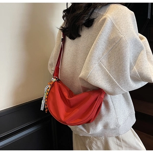 Detail of red crescent nylon crossbody bag with decorative graphic logo strap and folds