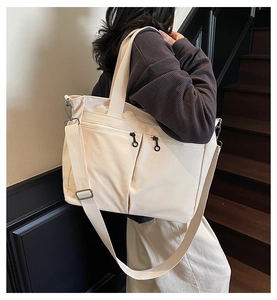 Close-up of cream canvas tote bag with dual front zippers and adjustable strap on a model