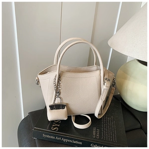Detail view of beige lychee texture bucket bag with mini charm on black book
