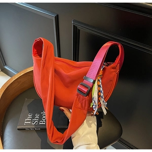Detail of red crescent nylon crossbody bag with wide strap and decorative pendant