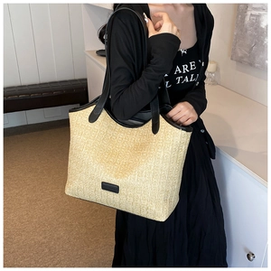 Close-up of a large beige woven straw tote bag with black leather straps on a model