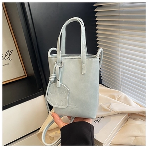Detail of light blue mini bucket bag featuring a bow logo and a matching cartoon charm