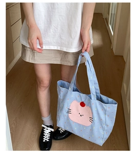 Détail du cabas en toile à carreaux bleus avec écusson chat rose et poignées supérieures