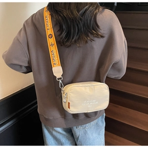 Detail of beige canvas crossbody bag with orange graphic strap and modern embroidery