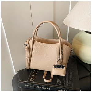 Detail of beige lychee pattern handbag with round handles and mini charm decoration