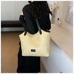 Detail of a large straw tote bag with black leather straps and fashion label decoration