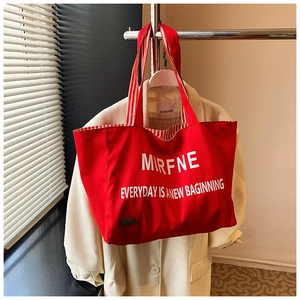 Detail of red canvas tote bag featuring white letters and striped ribbon handle