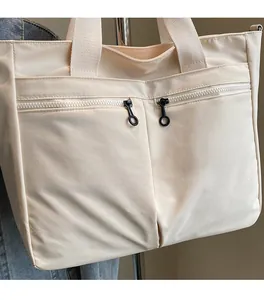 Close-up of off-white tote bag with dual zipper front pockets and fabric handles