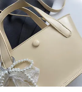 Dettaglio della borsa a secchiello beige con elegante catena di perle e decoro in pizzo