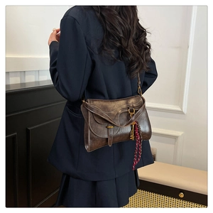 Deep brown retro saddle bag with golden key pendant shown on a model in a minimal interior