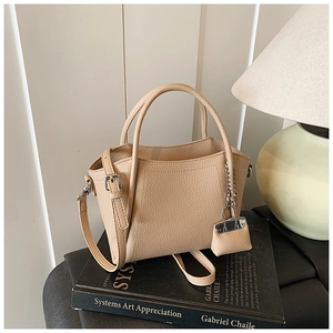 Detail of beige lychee textured leather bucket bag with silver chain and mini pouch charm