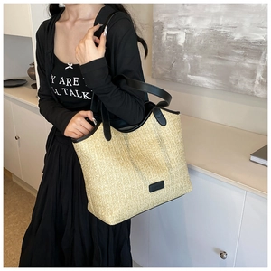 Detail of beige straw tote bag with black leather handles and woven texture on model