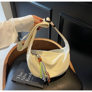 Close-up of cream canvas crescent bag with colorful letter fringe tassel and wide strap