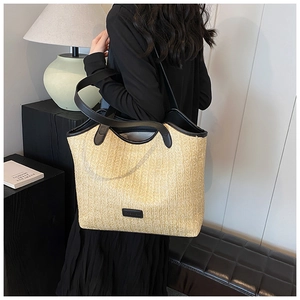 Detail of woven straw tote bag with black leather handles and fashion logo patch