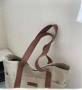 Detail of beige canvas tote bag with brown woven handles and leather patch accent