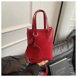 Detail view of mini red bucket bag with dog charm and embossed logo on glossy leather