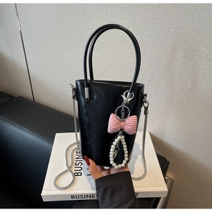 Detail der schwarzen glänzenden Beuteltasche mit rosa Karo-Schleife und Perlen-Anhänger