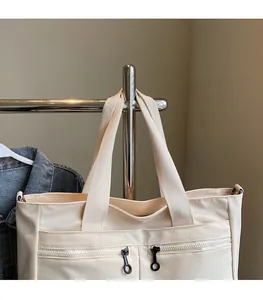 Detail of off-white tote bag showing wide fabric shoulder strap and front zipper pockets