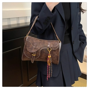 Detailed side view of a brown saddle bag featuring white stitching and tassel charm