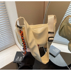 Close-up of cream crossbody dumpling bag with wide fabric strap and colorful woven charm