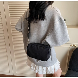Detailed back view of a black nylon camera bag with wide printed shoulder strap on model