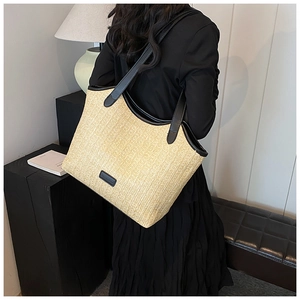 Detail of woven straw tote bag with black leather straps shown on a female model