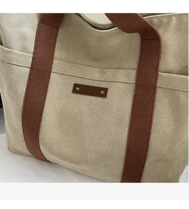 Detail of beige canvas tote bag with brown woven handles and stitched leather label