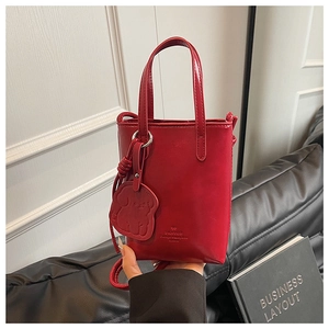 Detailed shot of a red leather crossbody bucket bag with a cute dog-shaped charm